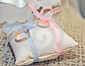 Two alliances knotted with bows on a small cushion. Focus on the ring with the pink bow.