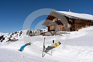 Two alpine skier and snowboarder laying back in snow with Swiss chalet in background