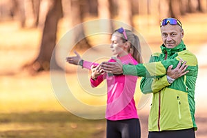 Two amateur athletes mature man and woman are warming up before jogging, doing upper body stretching in the park