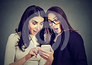 Two amazed women roommates watching offers on line on a smart phone.