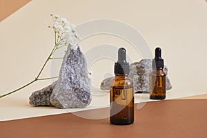 two amber glass bottles with pipette and stones on beige brown background