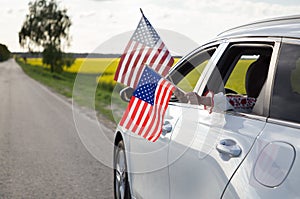 Two American flags hanging out of the window of a white car