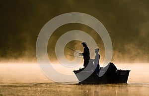 Due pescatori di pesca in una nebbiosa illuminata dal sole del lago.