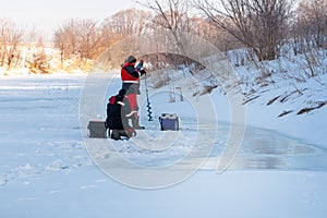 Two anglers on the ice of the river are preparing gear for ice fishing