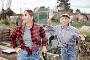 Two angry casual women neighbors of different ages arguing during the vegetable garden season on sunny day of spring