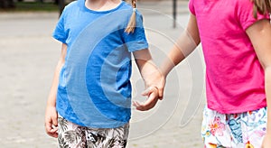 Two anonymous school age children, sisters, siblings together, one girl grabbing, taking other girls hand, kids holding hands