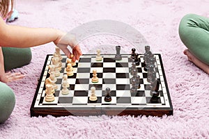 Two anonymous unrecognizable school age children, little girls playing chess in their room at home, chess board on the ground