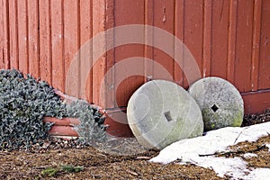 Two antique millstones leaning against a rustic red wooden build