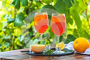 Two Aperol spritz cocktail in big wine glass with oranges, summer Italian fresh alcohol cold drink. Sunny garden with vineyard