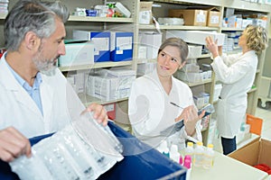 Two apothecaries in pharmacy next to shelf with prescriptions