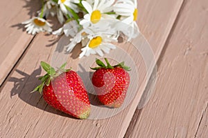 Two appetizing ripe strawberries on wooden background awith stripes nd white chamomile