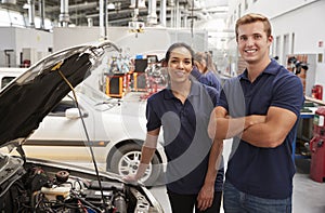 Two apprentice mechanics looking to camera beside a car
