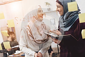 Two arab women working in office. Coworkers are taking notes on glass board.