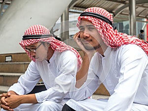 Two Arabic muslim wear white shirt sit on the stairs worried about business is not successful