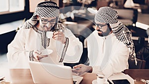 Two arabs drink coffee and looking on laptop