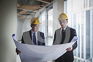 Two architects in hardhats examining a blueprint in an office building