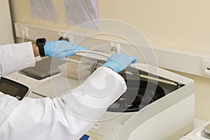 Two arms of a lab technician and both hands with blue nitril gloves closing a centrifuge.