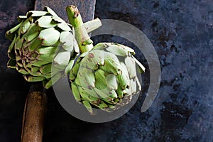 Two artichokes Cynara cardunculus, vegetables, old chopping knife, dark background.