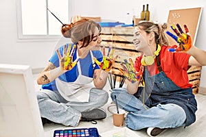 Two artist student women smiling happy showing painted hands at art school