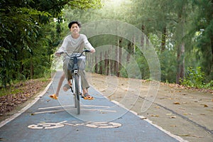 Two asian boys smiling and riding a bicycle on road and bicycle symbol in pine forest at outdoor park for concept of activity.