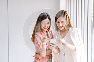 Two Asian business women looking at the smartphone screen using smart phone for online shopping, internet.