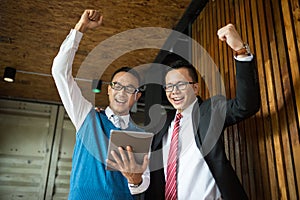 Two Asian businessman stand and looking at tablet, they cheerful and celebrated his successful in mission.