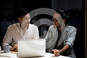 Two asian businessmen using computer to discuss work in the office at night