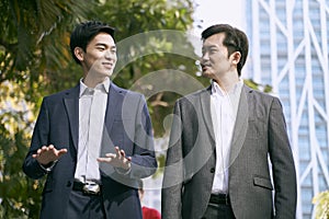 Two asian businessmen walking talking on street