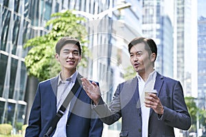 Two asian businessmen walking talking on street