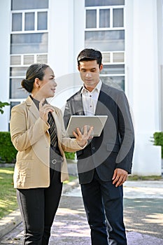 Two asian businesspeople are talking having a conversation while walking along the building