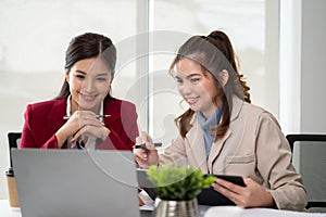 Two Asian businesswomen are looking at a laptop screen, discussing and planning work