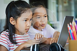 Two asian child girl students study online with teacher by video call together. Siblings are homeschooling with computer laptop