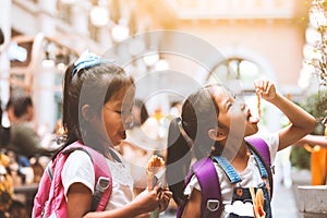 Two asian child girls with backpack eating pancake together after school in the school