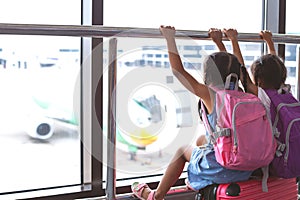 Two asian child girls with backpack looking at plane and waiting for boarding in the airport together