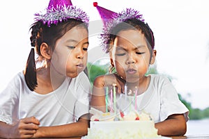 Two asian child girls celebrating birthday and blowing candles on birthday cake