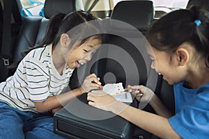 Two asian child girls eating dessert together while traveling in the car.