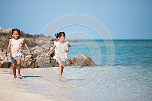 Two asian child girls having fun to play and run on beach together in summer vacation