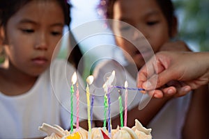 Two asian child girls lighting candle on birthday cake together in birthday party