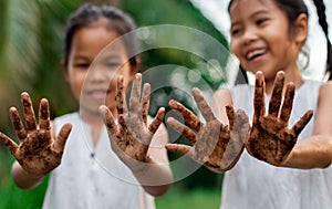 Two asian child girls showing dirty hands after planting the tree together in the garden