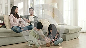 two asian children playing building blocks in front of parents at home