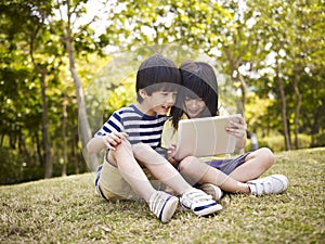 Two asian children using tablet outdoors