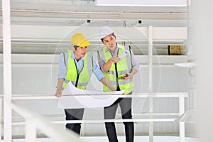 Two Asian contracting engineers wearing safety equipment while inspecting and discussing inside the warehouse photo