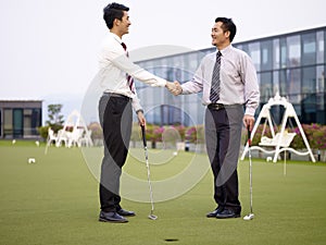 Two asian corporate executives shaking hands on golf course
