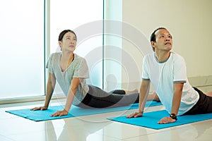 Two Asian couple husband wife practice Yoga pose Cobra or Bhujangasana on blue mat