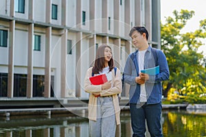 Two Asian couple university students walking and talking to class in walkway on a beautiful sunny day in campus