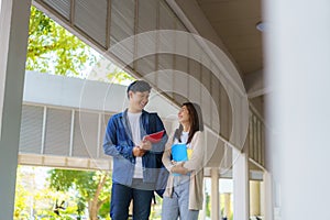 Two Asian couple university students walking and talking to class in walkway on a beautiful sunny day in campus