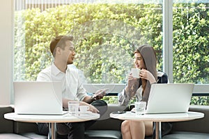 Two asian coworkers use laptop and smartphone work together having coffee in afternoon