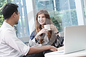 Two asian coworkers use laptop and smartphone work together having coffee in afternoon