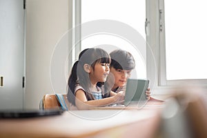 Two Asian Elementary school kids using digital tablet