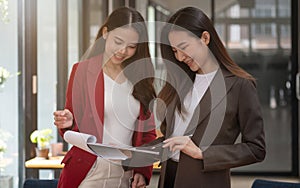 Two asian female collegues standing next to each other in an office, business meeting discussion concept